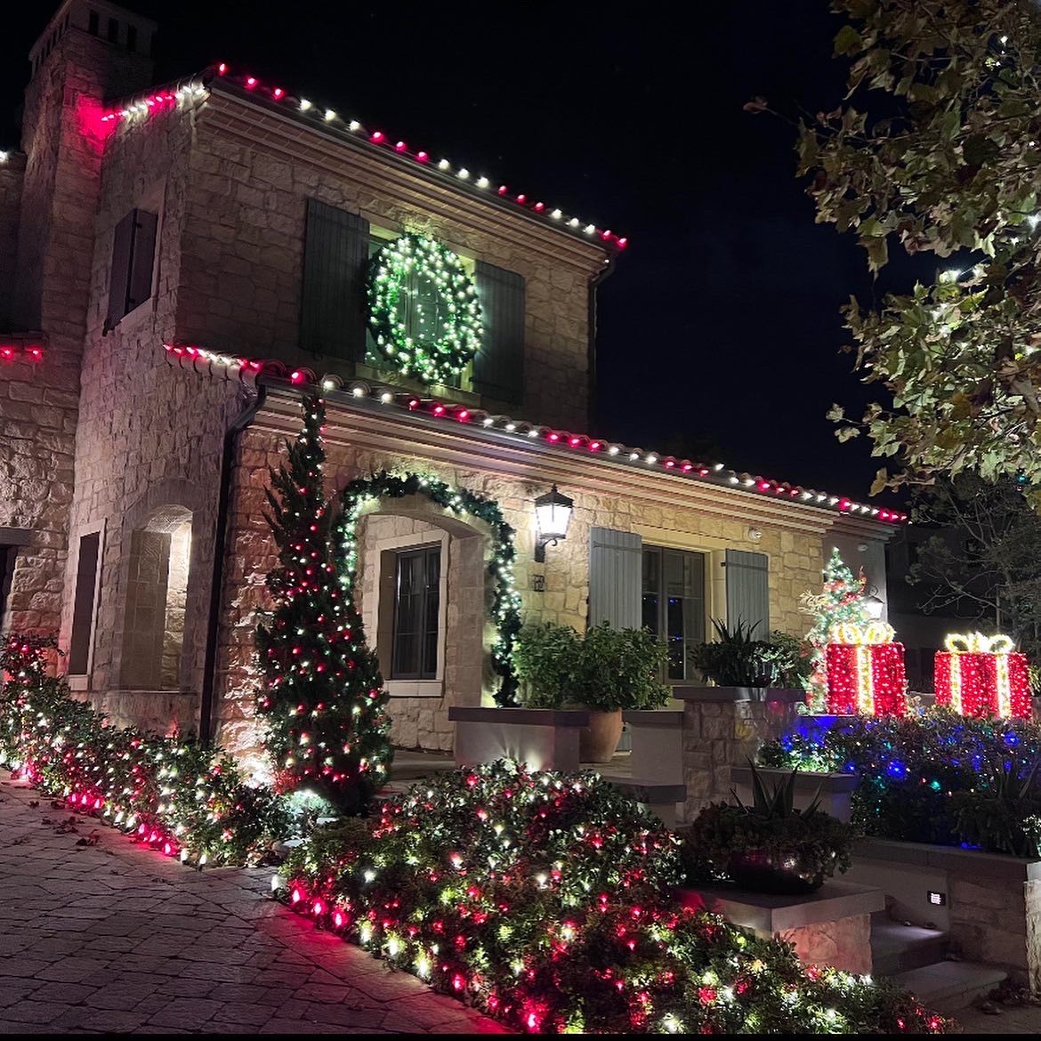 Garland, a lit wreath, and red and white lights surrounding a stone entryway