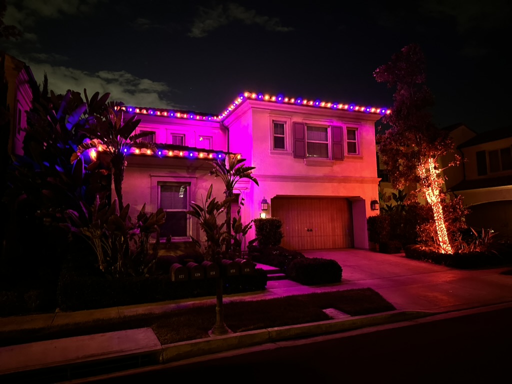 Home lit with vivid violet uplighting, orange tree lights and an orange-and-violet roofline