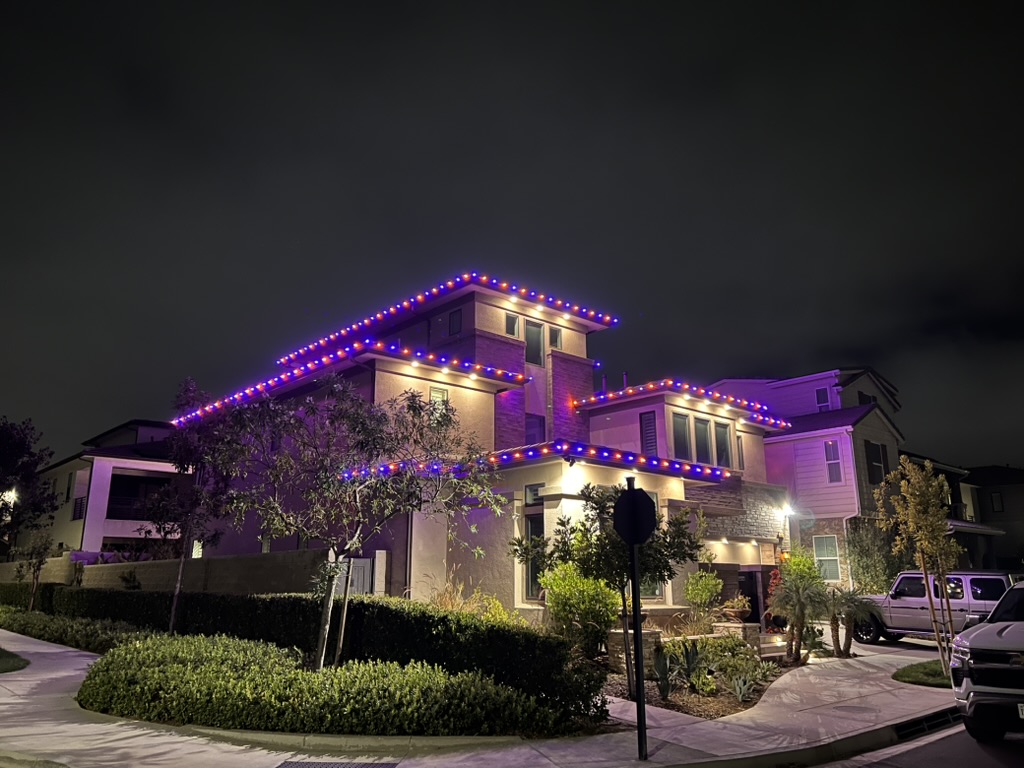 Two-story home outlined with alternating orange and violet Halloween lights at night